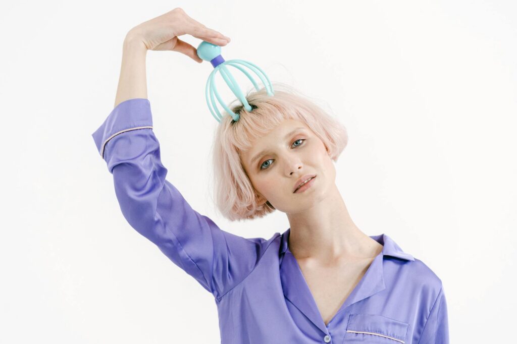 a woman in purple sleepwear massaging her head while looking at the camera