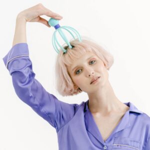 a woman in purple sleepwear massaging her head while looking at the camera